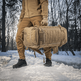 Person bærer M-Tac Rygsæk Gen.II Elite Large i sneklædt skov, fremstillet af slidstærk Cordura med stilrent design.