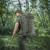 Mand med M-Tac Rygsæk Gen.II Elite Large i skovterræn, ergonomisk design med holdbar Cordura, ideel til outdoor og våbentransport.