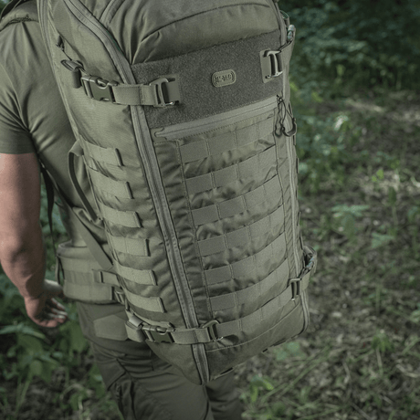 Person iført M-Tac Rygsæk Gen.II Elite Large i naturen, viser rygsækkens holdbare Cordura design og rummelige opbevaringsmuligheder.