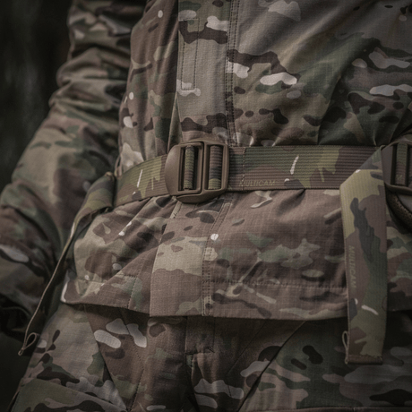 Nærbillede af militær uniform med camouflagemønster, fokuseret på bælteområdet i skovmiljø.