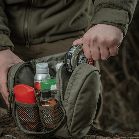Person holder M-Tac Toilettaske Elite Gen.II med rejsetoiletartikler såsom shampoo, lotion og tandpasta udendørs.