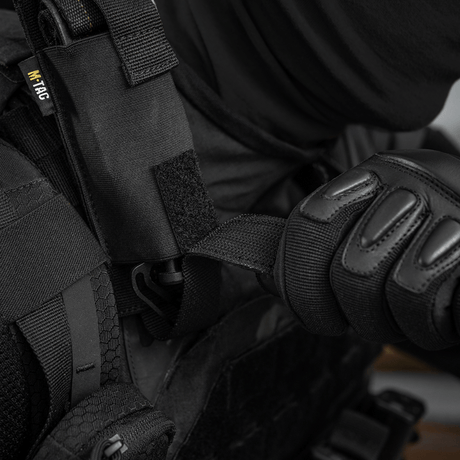 Person iført sort beskyttelsesudstyr bruger M-Tac Tourniquet Pouch Elastisk med MOLLE Gen.II fastgjort til vesten