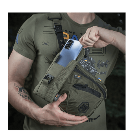 Mand med M-Tac Smartphone Lomme Elite Large Hex i mørkegrøn farve holder en smartphone.