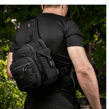 Mand bærer en sort M-Tac Smartphone Lomme Elite Large Hex lavet af CORDURA HEX-materiale. Stilfuldt design, perfekt til telefoner op til 6,5 tommer.