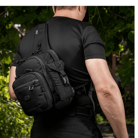 Mand bærer en sort M-Tac Smartphone Lomme Elite Large Hex lavet af CORDURA HEX-materiale. Stilfuldt design, perfekt til telefoner op til 6,5 tommer.