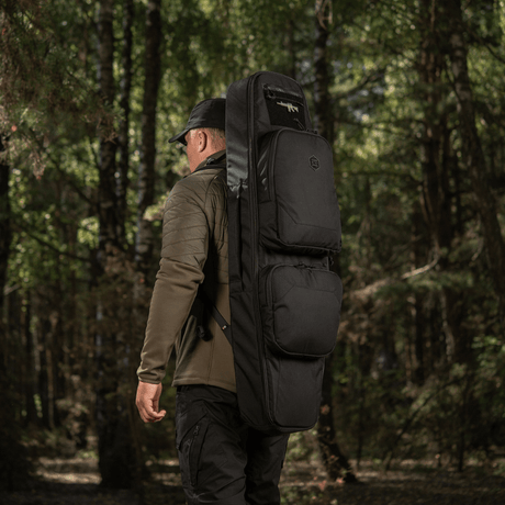Mand bærer M‑Tac Gun Backpack Case 105 cm Elite Hex gennem skoven, ideel til AR-15 og AK karbiner transport. Cordura 500D materiale.