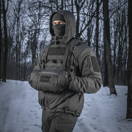 Person iført M-Tac Taktisk Håndvarmer Elite i skov med snebaggrund, holdende hænderne varme i det kolde vejr.