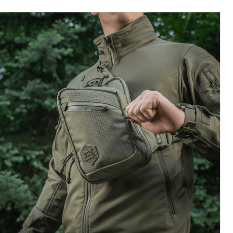Person iført M-Tac Sling Pistoltaske Elite Hex udendørs i komfortabel og holdbar taske med justerbar rem og rummelige rum.