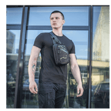 Mand iført M-Tac Sling Pistoltaske Elite Hex foran glasbygning, viser alsidighed og stil