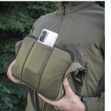 M-Tac Admin Taske Elite i Cordura stof, vist med en smartphone i lommen, justerbar skulderrem og solid konstruktion, udendørs baggrund.