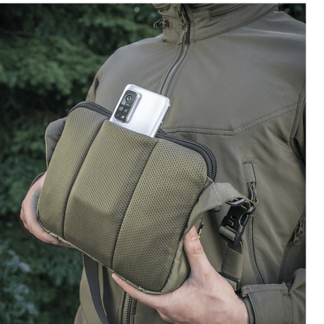 M-Tac Admin Taske Elite i Cordura stof, vist med en smartphone i lommen, justerbar skulderrem og solid konstruktion, udendørs baggrund.