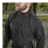 Mand bærer M-Tac Mission Pack Elite-rygsæk i skovområde, viser holdbarhed og stilfuldt design i Cordura 1000D stof.