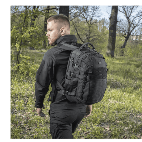 Mand bærer M-Tac Mission Pack Elite rygsæk i naturen, fremhæver det ergonomiske design og slidstærk Cordura 1000D materiale.