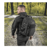 Mand bærer M-Tac Mission Pack Elite rygsæk i skovmiljø, fremstillet af slidstærkt Cordura 1000D med MOLLE LASER CUT-system.