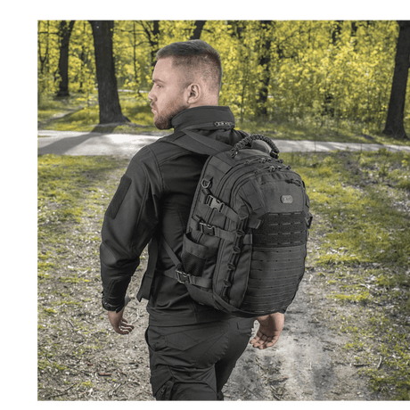 Mand bærer M-Tac Mission Pack Elite rygsæk i skovmiljø, fremstillet af slidstærkt Cordura 1000D med MOLLE LASER CUT-system.