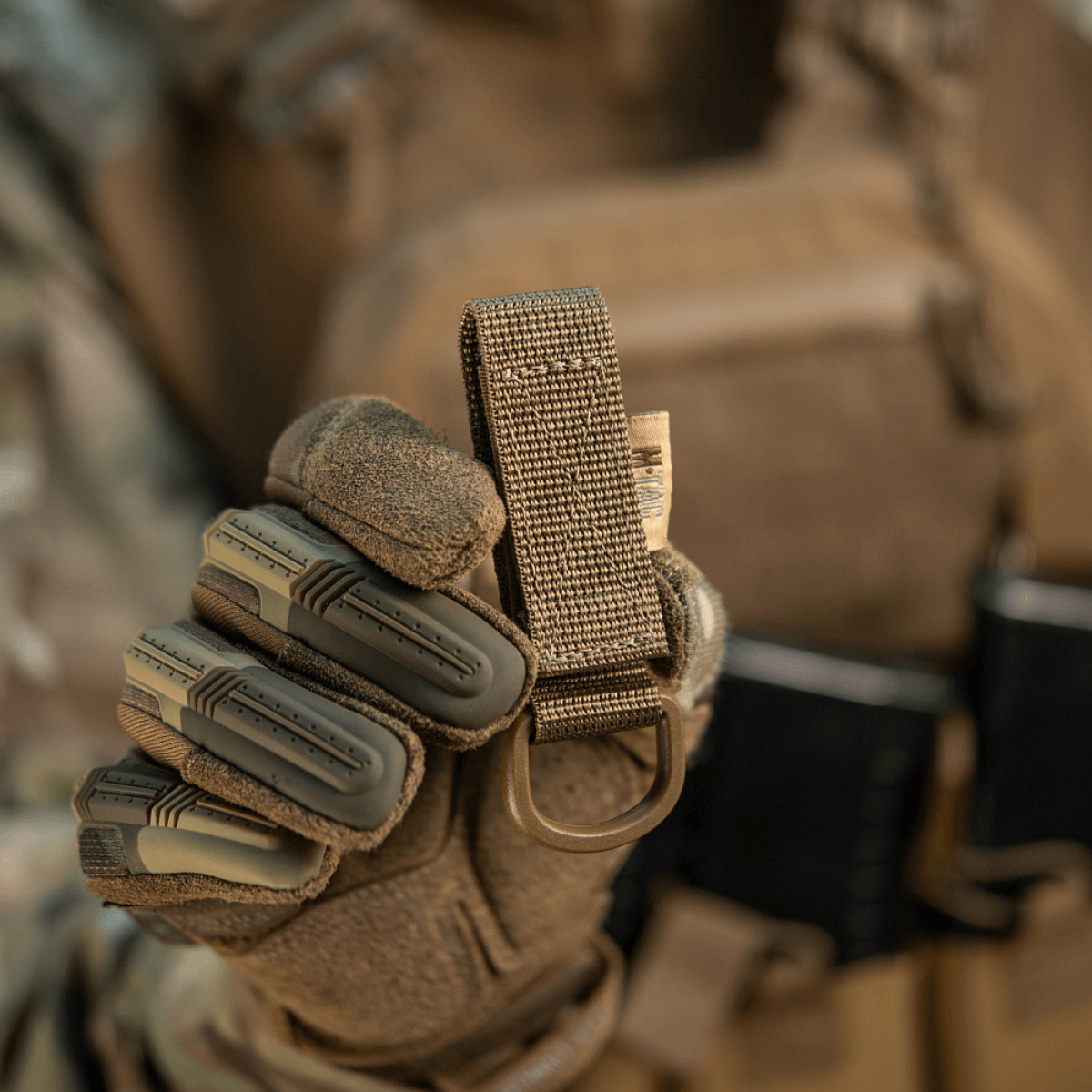 M-Tac Fastgørelse med D-ring i gloved hand for MOLLE gear attachment, ideal for tactical use with secure Velcro closure.