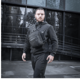 Mand med M-Tac Cross Taske Slim Elite Hex iført sort tøj foran moderne bygning