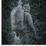 M-Tac Rygsæk Large Elite Hex Gen. IV i et skovmiljø, designet til bæring af våben og beskyttelse med holdbart Cordura-materiale.