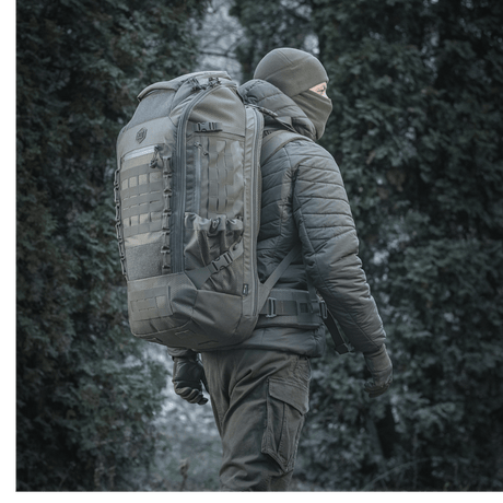 M-Tac Rygsæk Large Elite Hex Gen. IV i et skovmiljø, designet til bæring af våben og beskyttelse med holdbart Cordura-materiale.