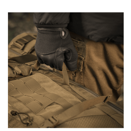 Bruger iført handsker holder M-Tac Rygsæk Large Elite Hex Gen. IV, lavet af slidstærkt Cordura 500D og Hex 1000.