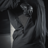 Person i sort jakke, der holder M‑Tac Pascover med "Passport"-tryk, praktisk til rejser.