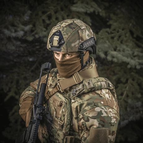 Soldat iført M‑Tac Hjelmcover Shroud Elite i MULTICAM, til TOR-D hjelme, med våben i skovlandskab.