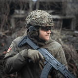 Soldat iført M‑Tac Vilha Hjelmcover FAST i Camouflage med riffel, klar til terrænudfordringer. Slidstærkt materiale, optimal pasform.