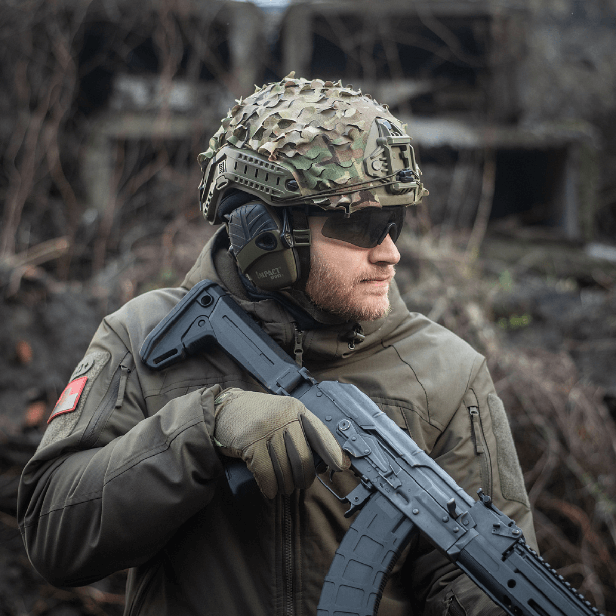 Soldat iført M‑Tac Vilha Hjelmcover FAST i Camouflage med riffel, klar til terrænudfordringer. Slidstærkt materiale, optimal pasform.