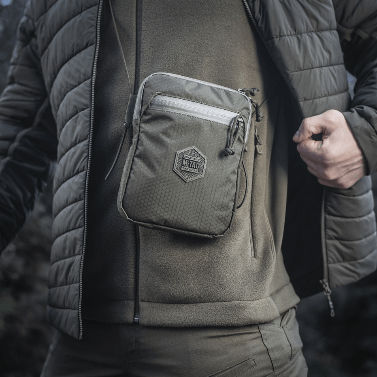 M‑Tac Pocket Bag Elite HEX bæres foran på en mand i udendørs beklædning, viser taskens kompakte og robuste design med YKK lynlåse.