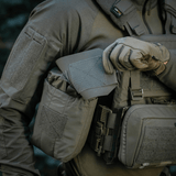 Person i taktisk tøj holder M‑Tac Medic Pouch Vertical Large Elite, innovativ medicintaske lavet af holdbart Cordura 500D-materiale.