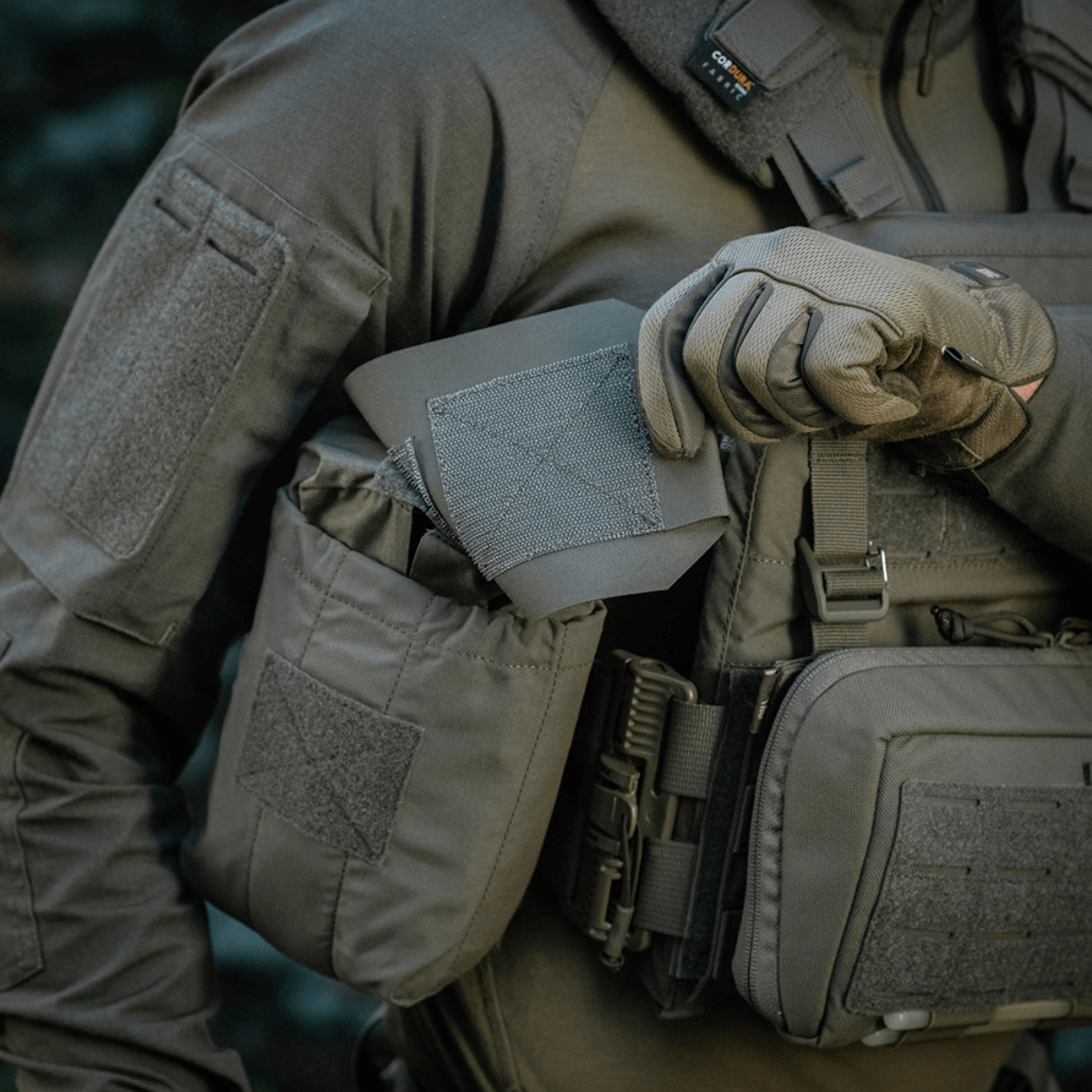 Person i taktisk tøj holder M‑Tac Medic Pouch Vertical Large Elite, innovativ medicintaske lavet af holdbart Cordura 500D-materiale.
