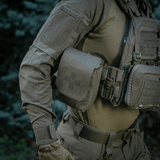 M-Tac Medic Pouch Vertical Large Elite monteret på taktisk vest i skov, robust opbevaring af førstehjælpsudstyr.