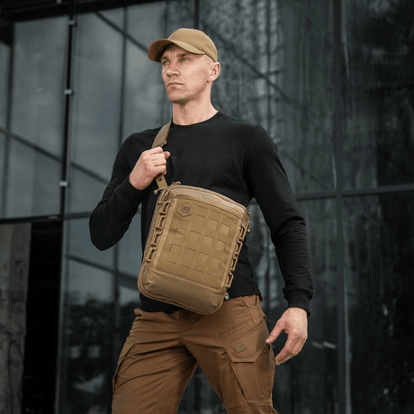 Mand bærer M-Tac Tablet Bag Laser Cut Hex foran kontorbygning, diskret skuldertaske til EDC og dokumenter.