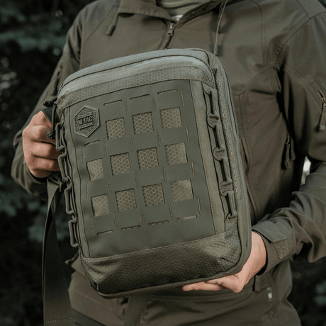 M-Tac Tablet Bag Laser Cut Hex med Laser Cut MOLLE-panel, lavet af Cordura-materialer, holdt af person i outdoor-miljø.