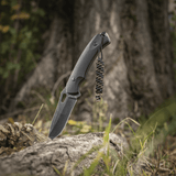 M-Tac Knife Lanyard Helix Skull i flettet paracord på sort kniv mod skovbund