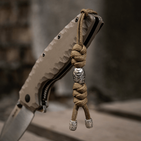 M-Tac Zeus Stainless Steel Lanyard med flettet paracord og dekorative perler på en kniv, brugt til hurtig adgang til udstyr.