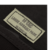 Etiketten på M-Tac Large Assault Pack Rygsæk i nærbillede, der viser produktets logo og navnetekst.