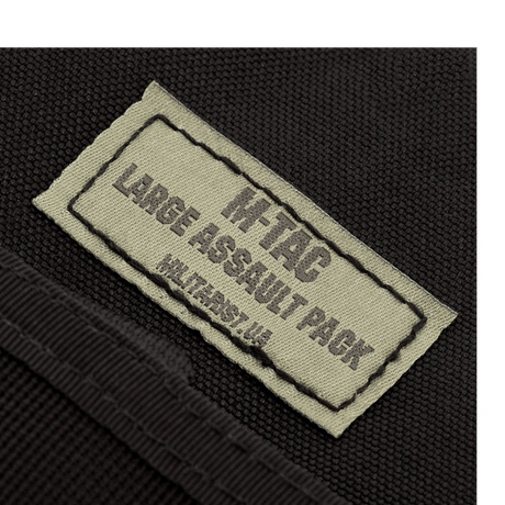 Etiketten på M-Tac Large Assault Pack Rygsæk i nærbillede, der viser produktets logo og navnetekst.