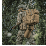 M-Tac Large Assault Pack Rygsæk i brug af en person i camouflagetøj i skovmiljø, med MOLLE-system og justerbare skulderremme.