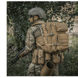 M-Tac Large Assault Pack Rygsæk med MOLLE-system, bæres af person i camouflageuniform under træer