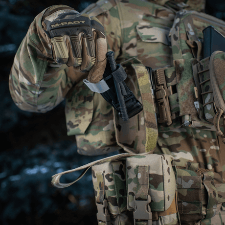 Militærpersonel holder M-Tac Lomme til Tourniquet Closed på taktisk vest, klar til nødsituationer.