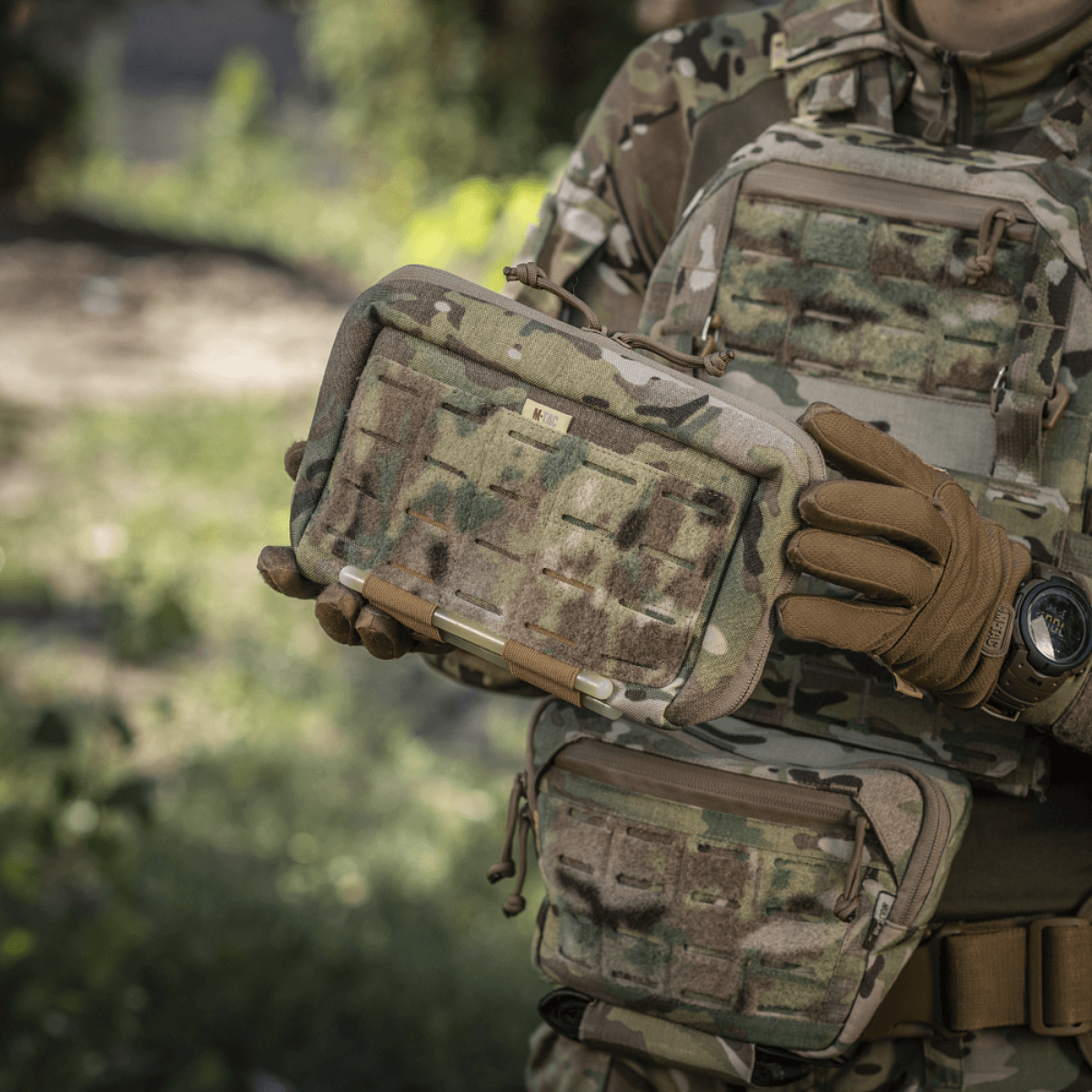 M-Tac Admin Pouch Large Elite holdt af person i kamuflageudstyr, viser holdbar og funktionel design til taktisk brug med velcro-paneler.