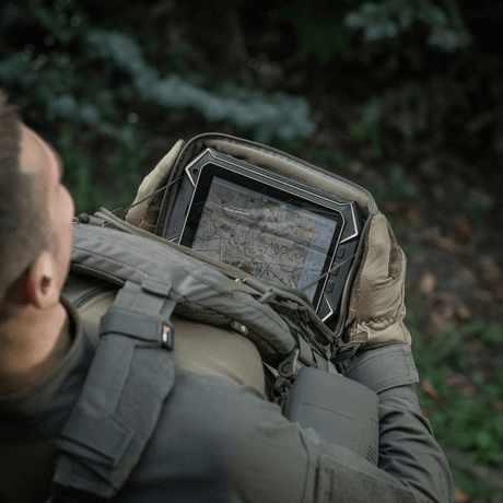 Person med M-Tac Admin Pouch Large Elite holder en tablet i en skov.