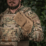 Soldat viser M-Tac Mediclomme Small Vertical Elite i hånden iført camouflageuniform og handsker.