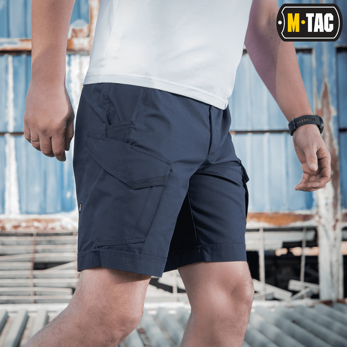 Mand iført M-Tac Shorts Aggressor Short i blå, ideel til taktisk brug på varme dage, fremstillet af elastisk polycotton rip-stop.
