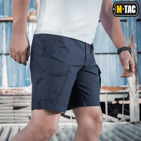 Mand iført M-Tac Shorts Aggressor Short i blå, ideel til taktisk brug på varme dage, fremstillet af elastisk polycotton rip-stop.