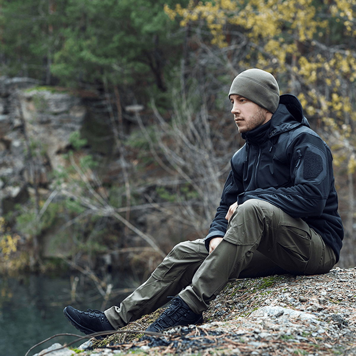 Mand iført M-Tac Norman Windblock Fleecejakke sidder udendørs i skovmiljø, tilpas til køligt vejr. Varm og vindtæt med Softshell-indlæg.