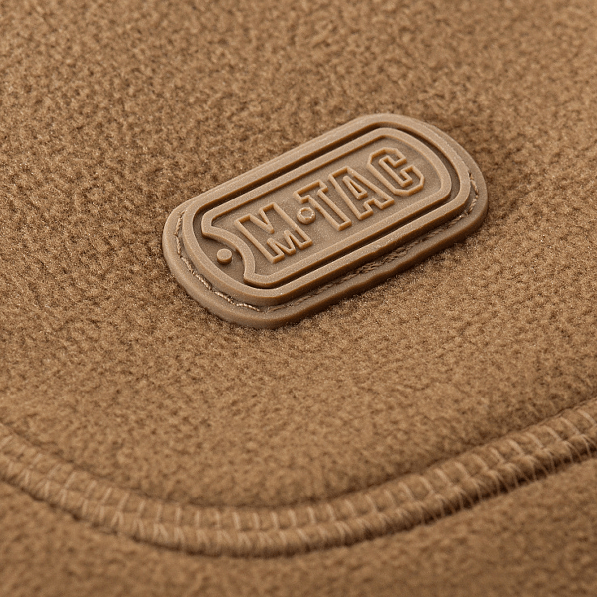 M-Tac Norman Windblock Fleecejakke emblem på brun fleece baggrund, detaljeret syning og logo synligt for kvalitet og stil.