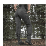 Kvinde bærer M-Tac Bukser Aggressor Dame Flex i skovmiljø, tætsiddende og vandafvisende design.