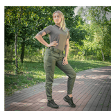 Kvinde iført M-Tac Bukser Aggressor Dame Flex på en sti i parken, ideel til træning og udendørs aktiviteter, fremhæver fleksibilitet og stil.